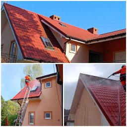 RENOWATOR KAROL PRZEŹDZIĘK - Czerwony dach domu z lukarnami czyszczony myjką ciśnieniową przez pracownika na drabinie. Widoczne zabrudzenia i strumień wody. Dachówka karpiówka.