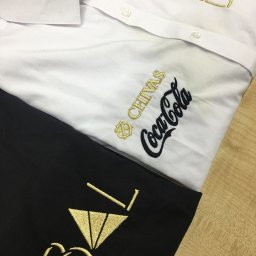 Everglow Paweł Świąć - Biała koszula i czarna bluza z wyhaftowanymi złotymi i czarnymi logotypami marek Chivas, Coca-Cola oraz inicjałami 'BVT'.