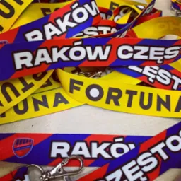 Stos pamiątkowych smyczy z nadrukami 'Raków Częstochowa' i 'Fortuna' w kolorach klubowych, z metalowymi karabińczykami.