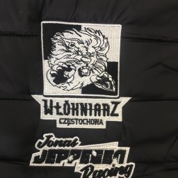 Everglow Paweł Świąć - Czarna kurtka z naszywkami: haftowany lew, napis 'Włókniarz Częstochowa' i logo 'Jonał Jeppesen Racing'.