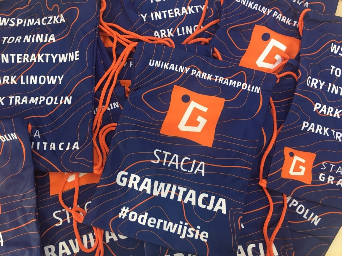 Stos niebieskich worków z pomarańczowymi sznurkami i nadrukiem logo Stacja Grawitacja z Kłobucka, prezentujących ofertę parku rozrywki.