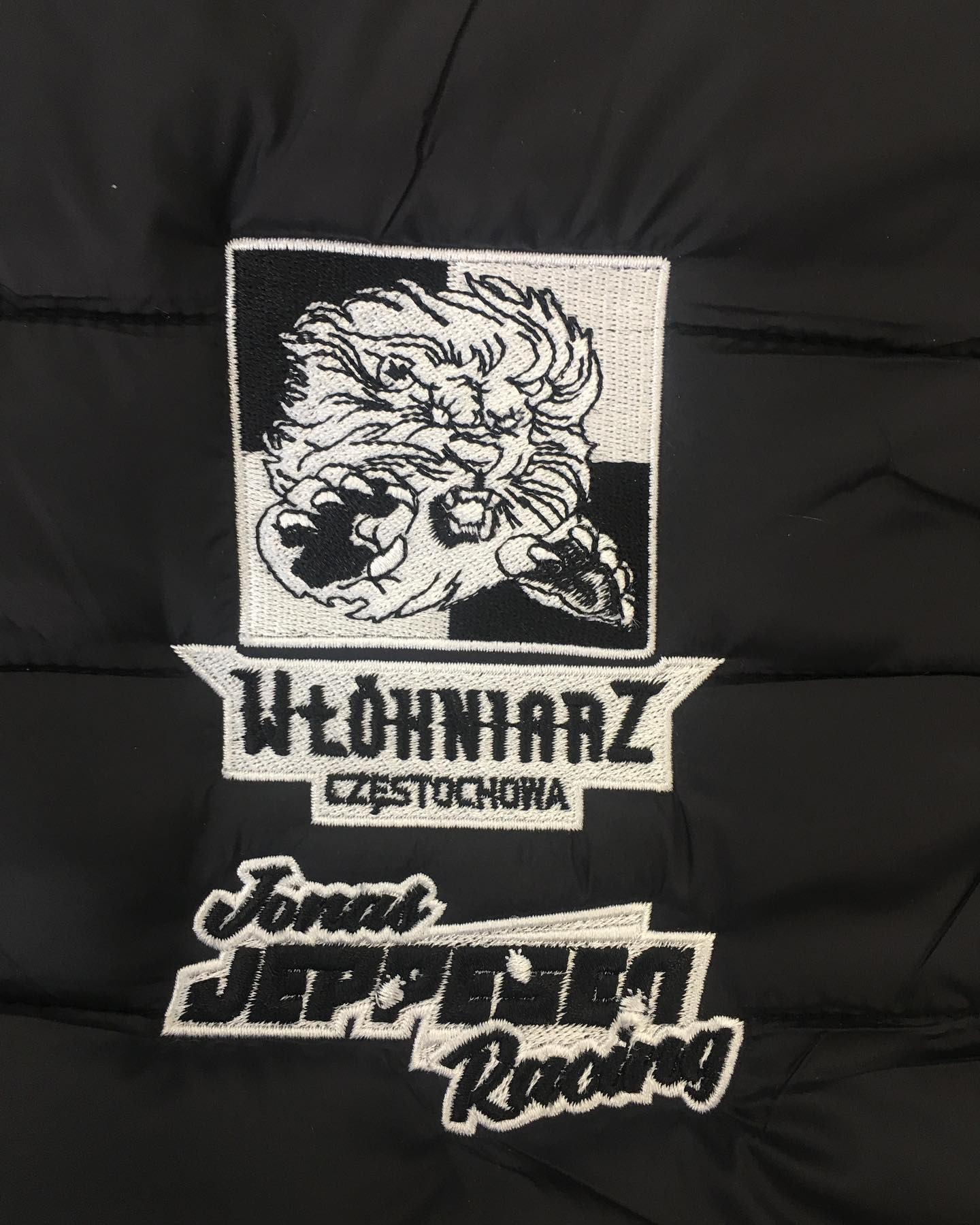 Czarna kurtka z naszywkami: haftowany lew, napis 'Włókniarz Częstochowa' i logo 'Jonał Jeppesen Racing'.