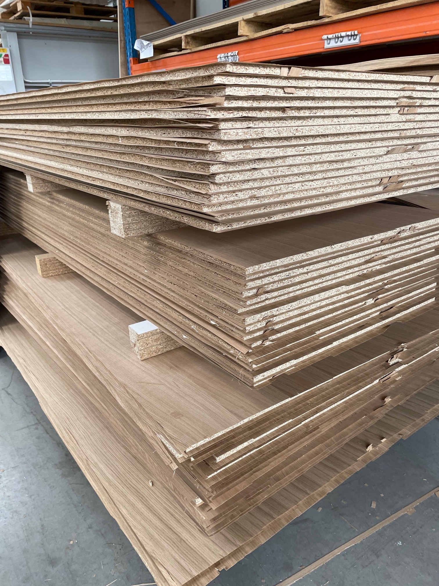 Stos płyt meblowych z okleiną drewnopodobną, oddzielonych przekładkami, składowanych na palecie w magazynie.
