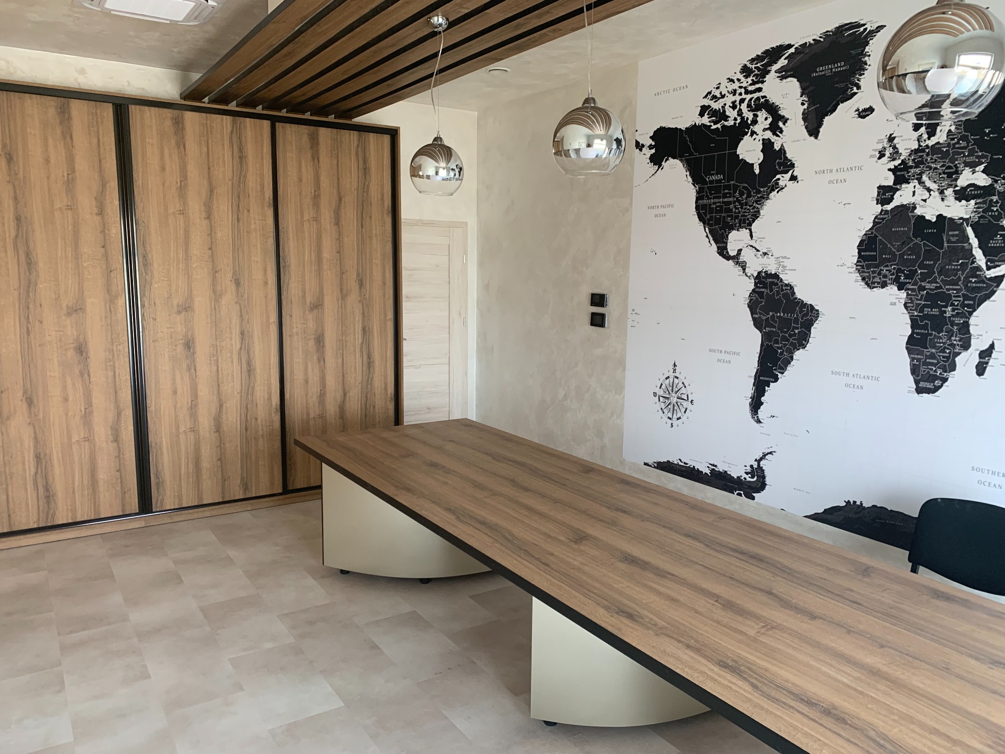 Szafa przesuwna z drewnopodobnymi frontami w nowoczesnym biurze z długim stołem konferencyjnym i mapą świata na ścianie.