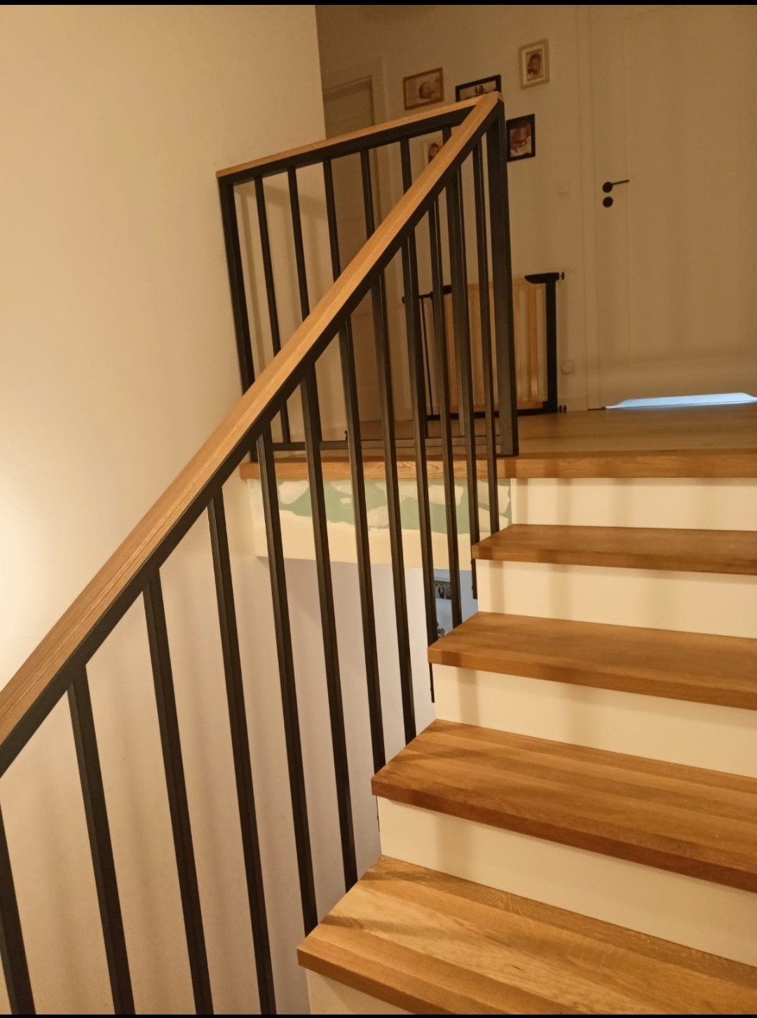 Nowoczesne schody drewniane z metalową balustradą w kolorze czarnym, drewniane stopnie z białymi podstopnicami, widok z dołu.