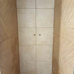 G-M-BUD - Wnętrze wykończone płytkami imitującymi marmur na ścianie frontowej oraz drewnopodobnymi panelami ułożonymi w geometryczny wzór na ścianach bocznych, widoczne dwa okrągłe uchwyty.