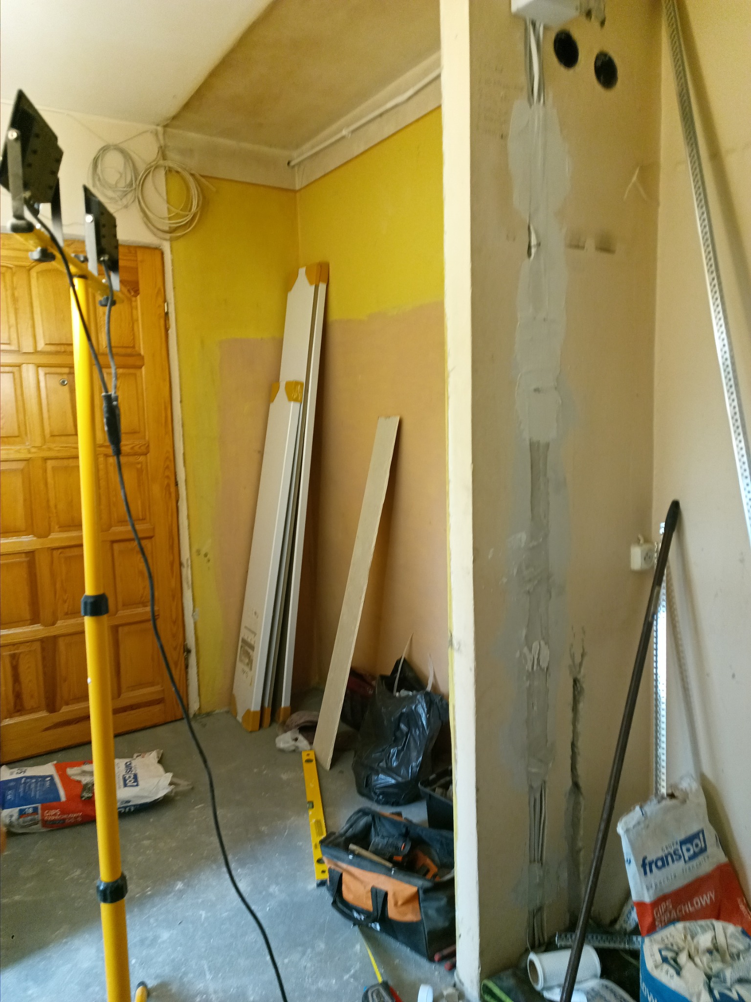 Przygotowania do prac wykończeniowych: widoczne ślady po instalacji elektrycznej wypełnione gipsem, narzędzia pracy, torba monterska, profile metalowe i worki z zaprawą gipsową w pomieszczeniu...