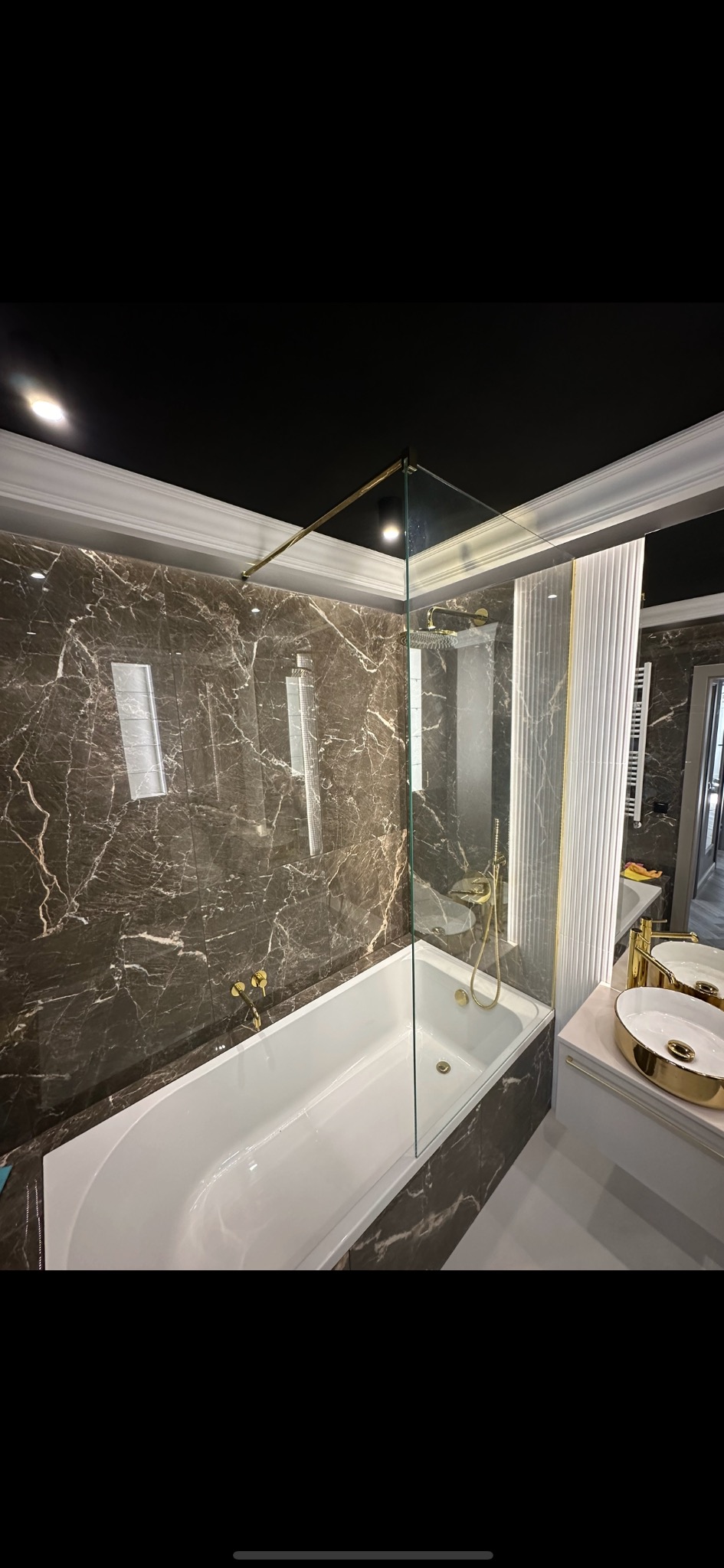 Nowoczesna łazienka z kabiną prysznicową ze szkła hartowanego, wykończona marmurowymi płytkami w odcieniach brązu i złota armatura.