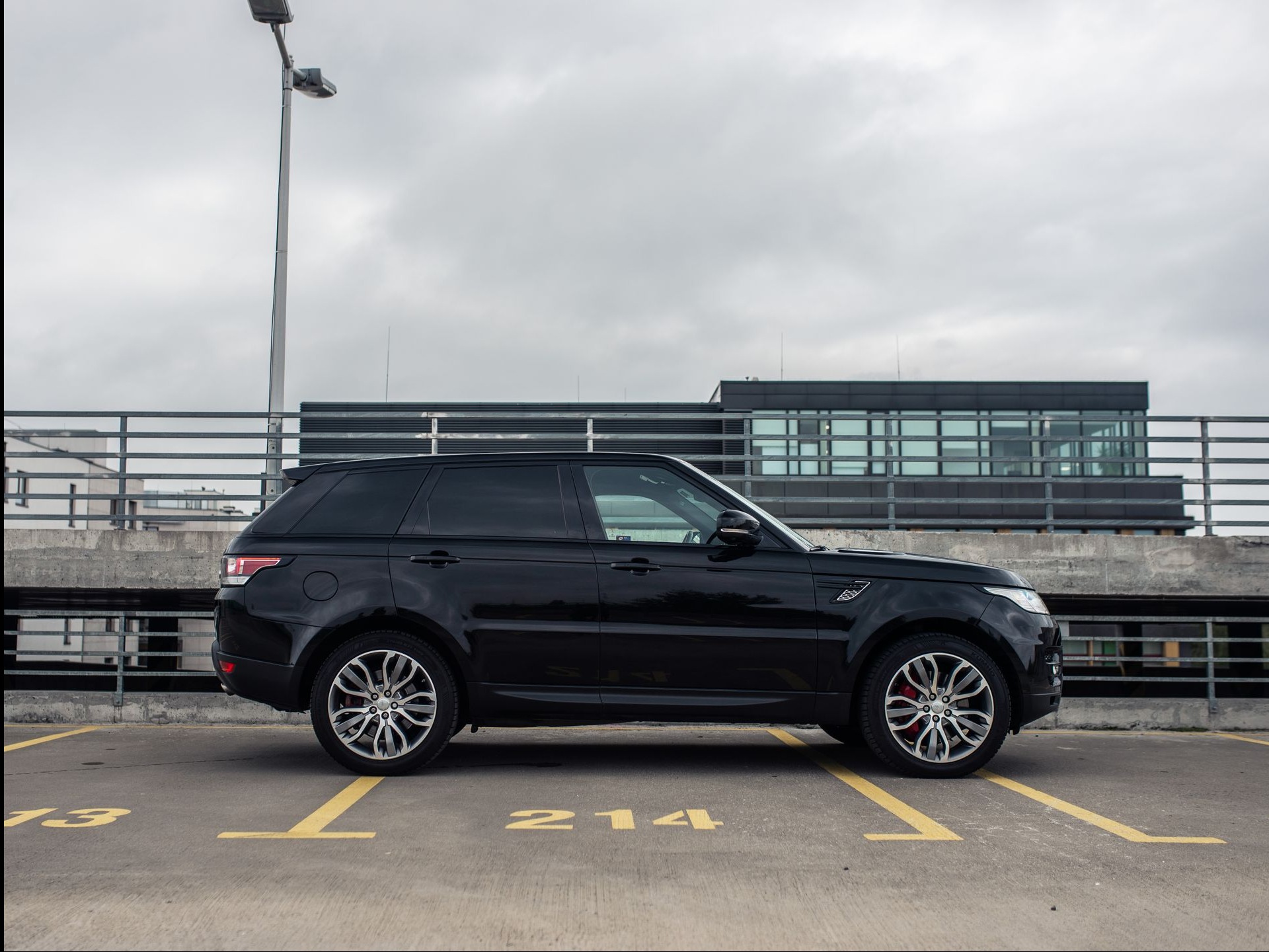 Czarny Range Rover Sport zaparkowany na parkingu wielopoziomowym, widok z boku, z numerem 214 na miejscu parkingowym i czerwonymi zaciskami hamulcowymi.