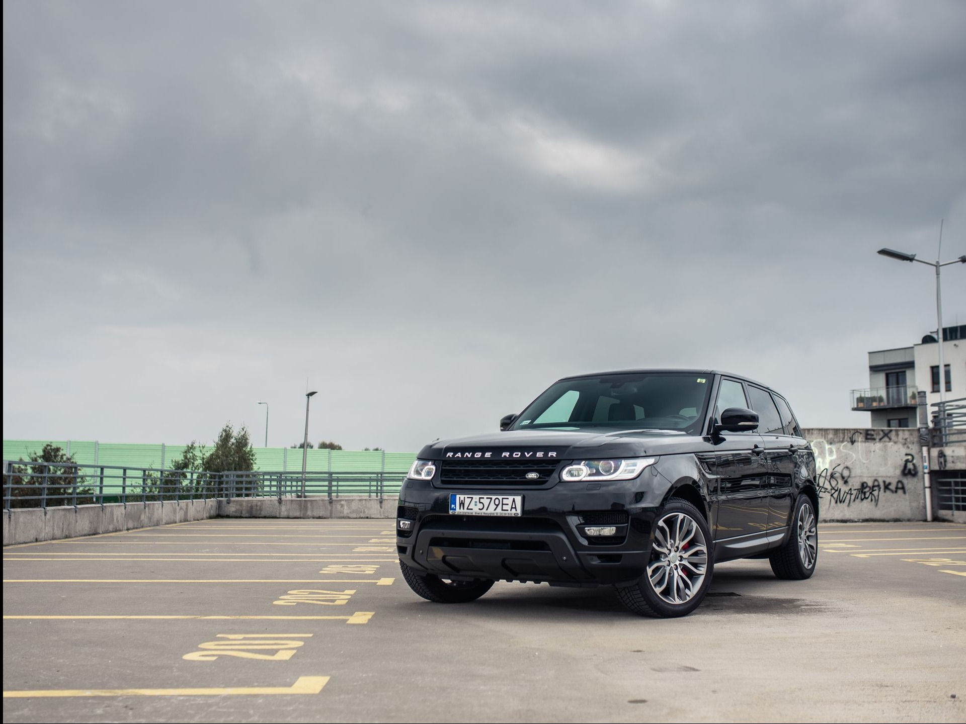 Czarny Range Rover Sport zaparkowany na parkingu wielopoziomowym w Warszawie, pochmurne niebo w tle.