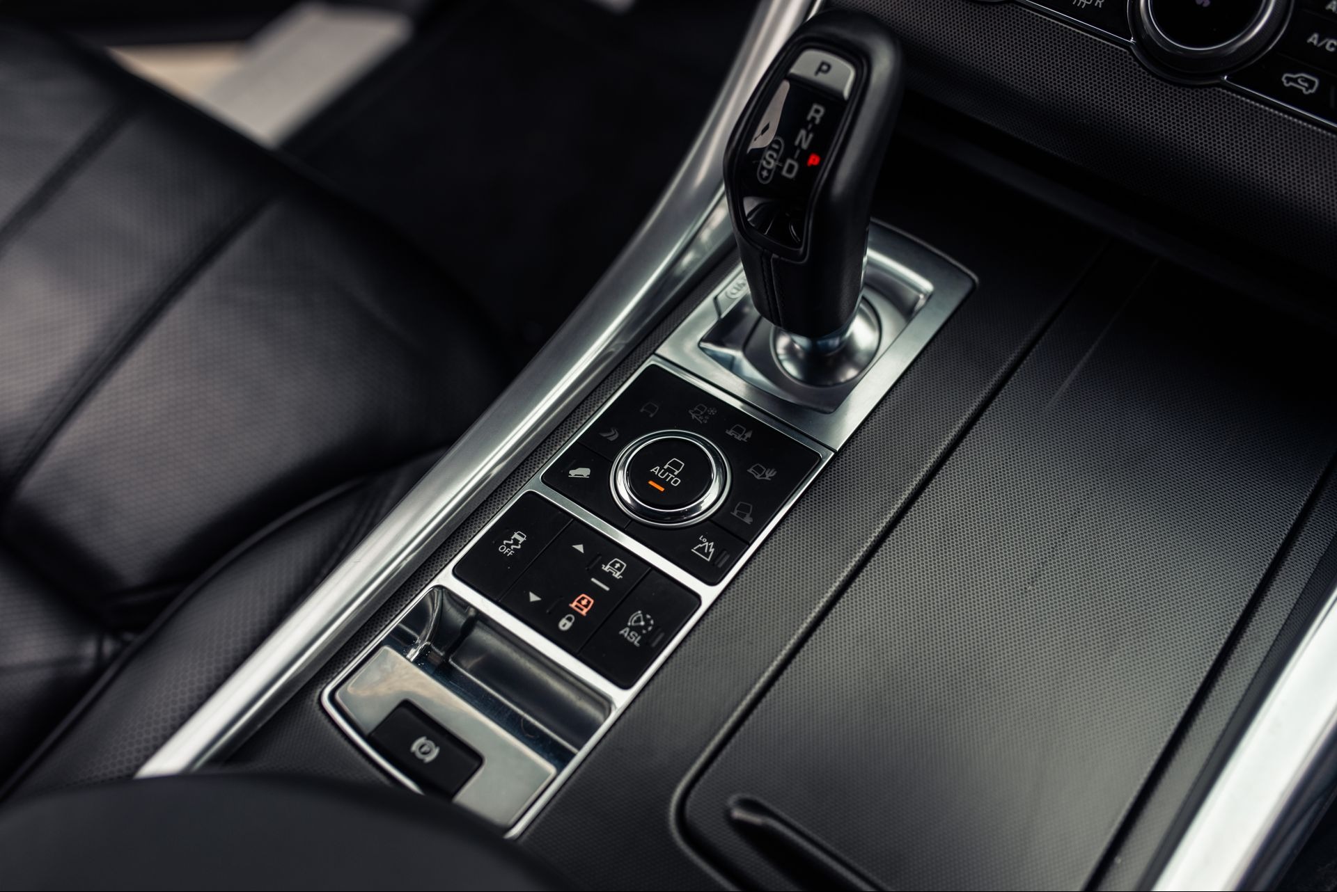 Wnętrze samochodu Range Rover Sport: dźwignia zmiany biegów w pozycji P, panel sterowania trybami jazdy z podświetlonym przyciskiem AUTO, czarne skórzane fotele z perforacją i srebrne wykończenia.