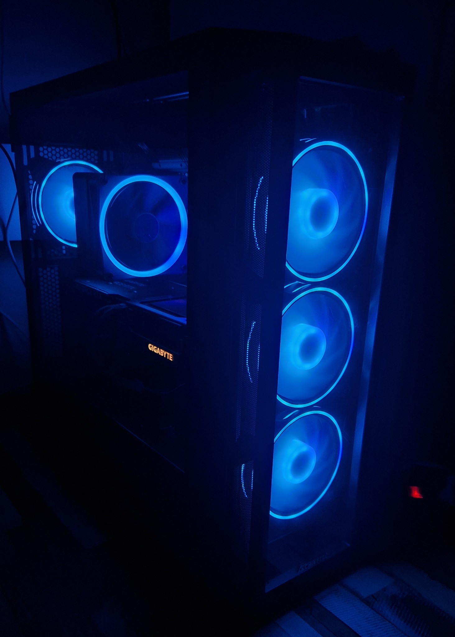 Komputer stacjonarny z podświetleniem LED w kolorze niebieskim, widoczna karta graficzna Gigabyte, wentylatory z podświetleniem na przednim panelu i wewnątrz obudowy.