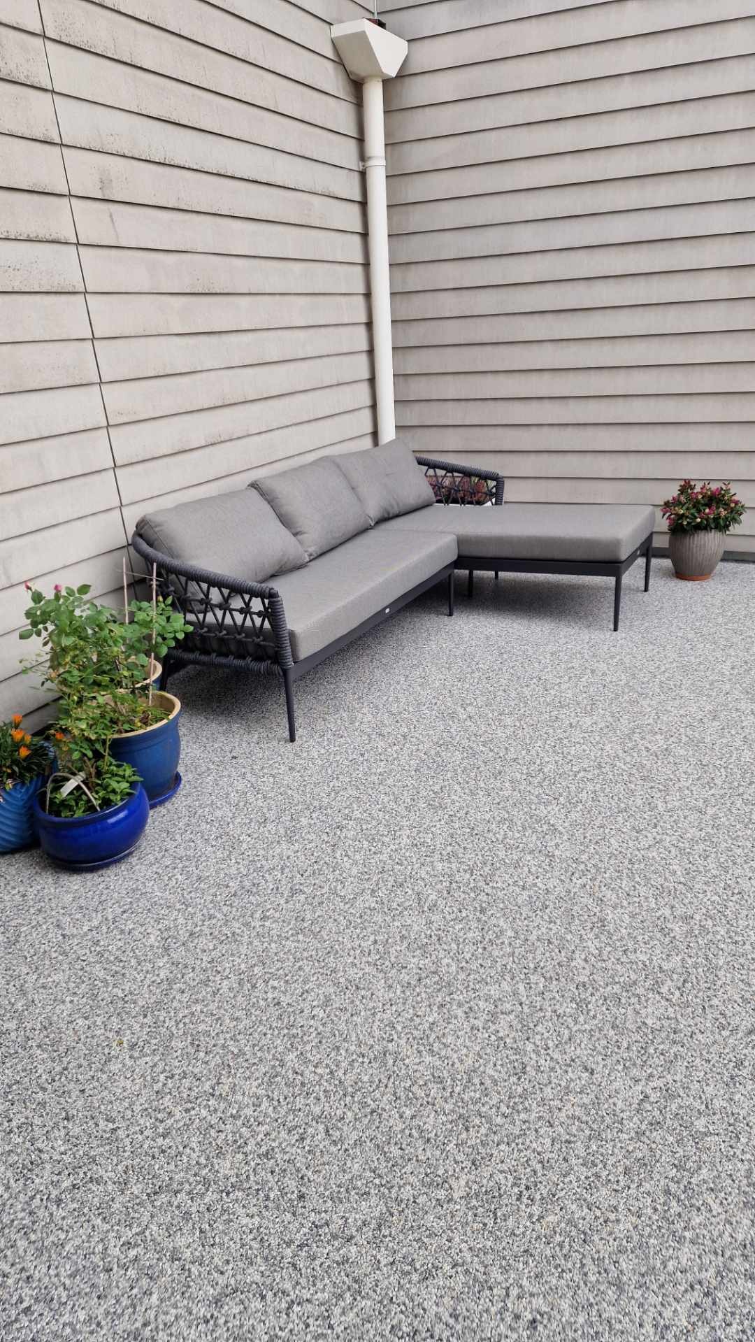 Szara posadzka na tarasie z meblami ogrodowymi i doniczkami, widok z góry. Jednolita, drobnoziarnista struktura powierzchni.