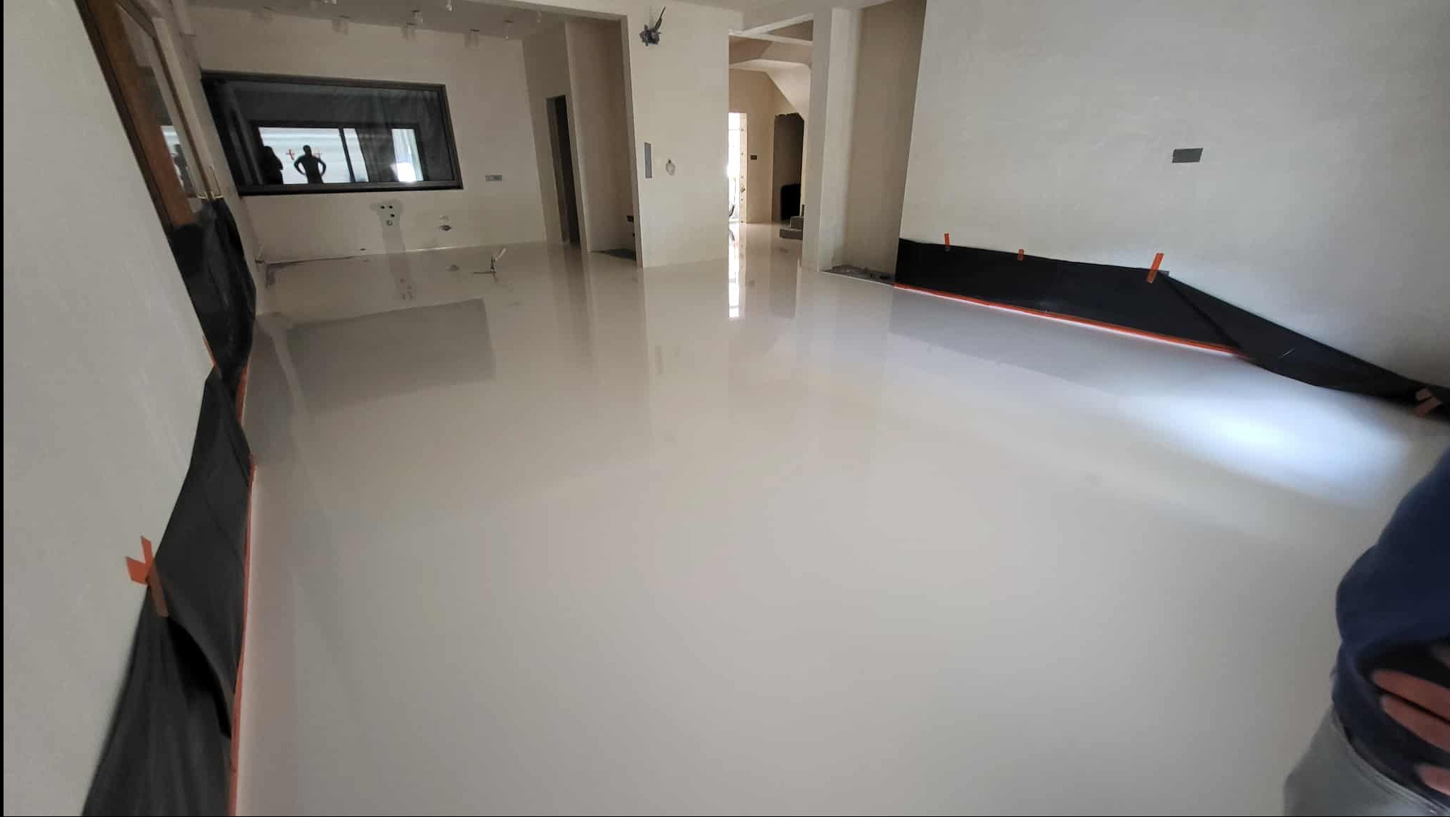 Błyszcząca, jasna posadzka w przestronnym wnętrzu z widocznymi zabezpieczeniami ścian. W oknie odbija się sylwetka osoby, co dodaje unikalności ujęciu.