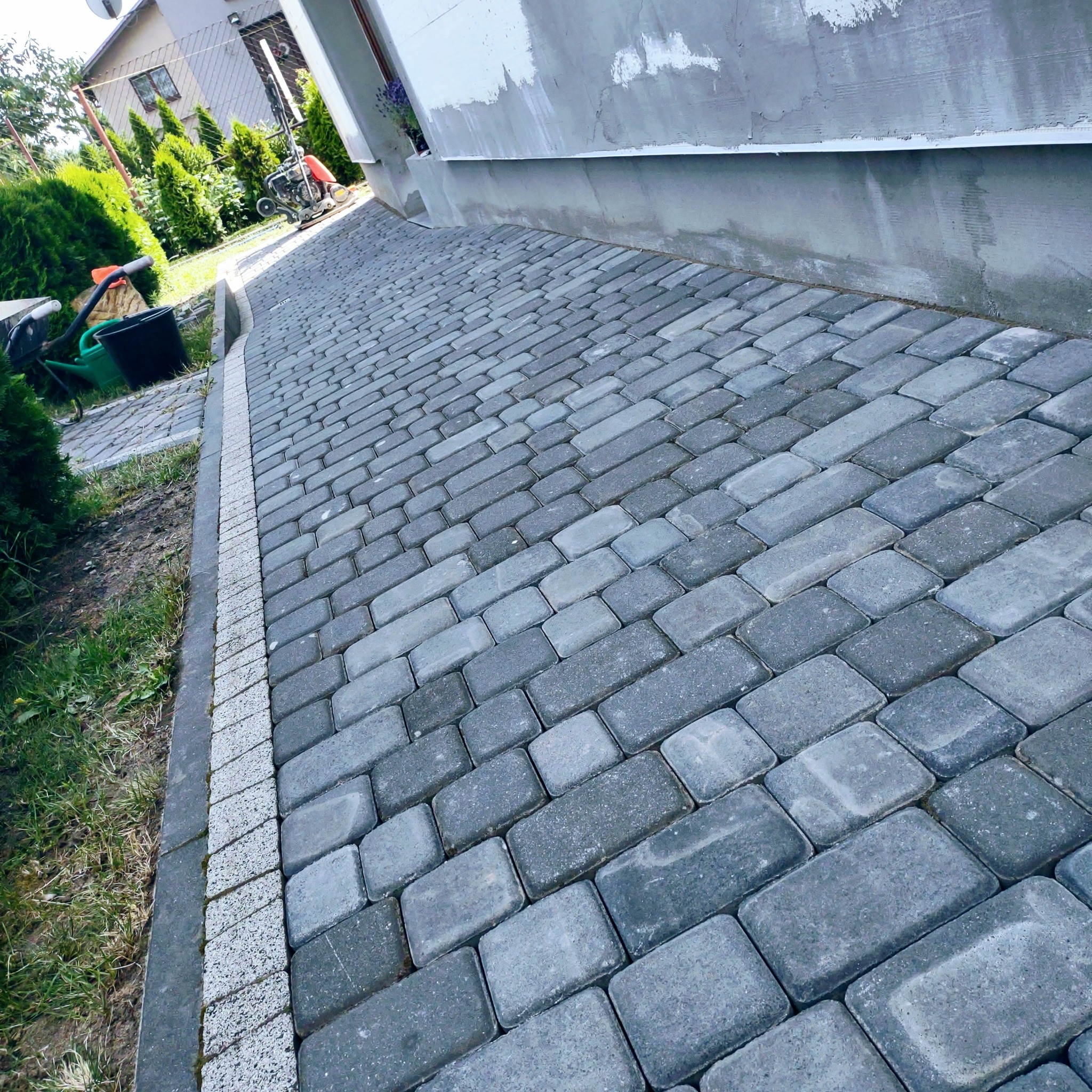 Ułożona szara kostka brukowa w Wyrzysku, widok z boku budynku, z obrzeżem z jasnej kostki, trawa i zieleń w tle.