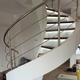 ELTREND Łukasz Balcerek - Spiralne schody z oświetleniem LED na stopniach i chromowaną balustradą w trakcie montażu w Tomaszowie Mazowieckim, widoczne narzędzia i materiały budowlane.