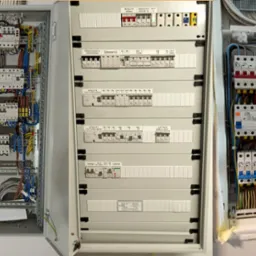 Trzy otwarte skrzynki rozdzielcze z widocznymi bezpiecznikami, przewodami i elementami zabezpieczeń, każda w innym stylu montażu i z różnymi komponentami, oświetlone światłem dziennym.