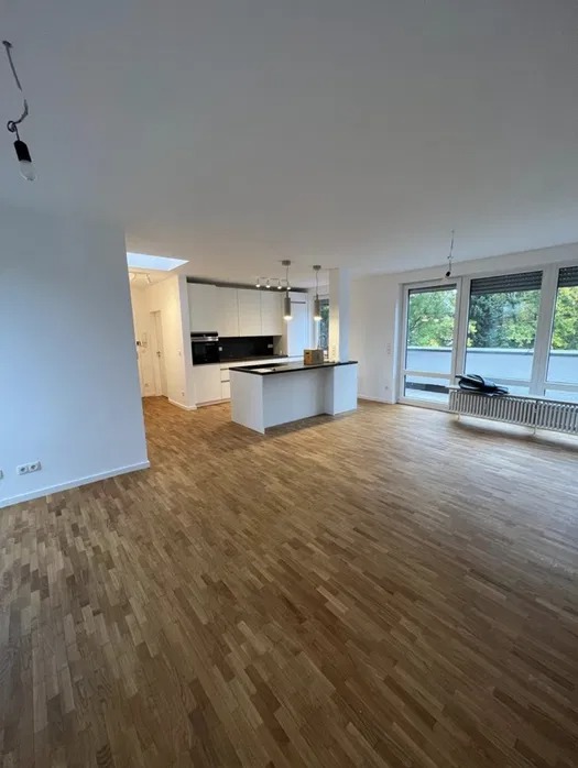 Przestronne wnętrze po remoncie z parkietem ułożonym w jodełkę, białe ściany i wyspa kuchenna z czarnym blatem, widoczne niedokończone podłączenie lampy sufitowej.