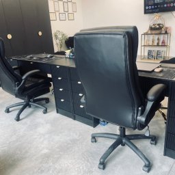 K&K Księgowość Sp. z o.o. - Nowoczesne biuro z czarnymi meblami: biurka z szufladami, skórzane fotele obrotowe. Na ścianie wiszą certyfikaty i dyplomy. W tle półka z dekoracjami.