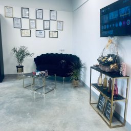 K&K Księgowość Sp. z o.o. - Eleganckie biuro z czarną sofą, złotymi stolikami i półką z dekoracjami. Na ścianie dyplomy i certyfikaty, a na półce tabliczki z motywacyjnymi hasłami.