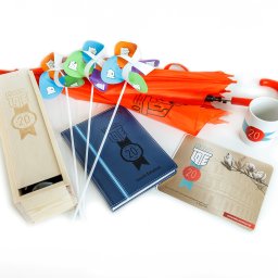 Agencja Promocyjno-Reklamowa SPOT s.c. Piotr Czerwiński, Wojciech Krawczyk - Zestaw gadżetów firmowych z logo LOT-e: drewniane pudełko, notatnik, podkładka, kubek, parasol i wiatraczki na białym tle.