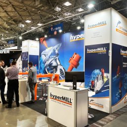 Agencja Promocyjno-Reklamowa SPOT s.c. Piotr Czerwiński, Wojciech Krawczyk - Stoisko targowe firmy HyperMILL z grafiką prezentującą proces obróbki metalu, widoczni ludzie w garniturach rozmawiający przy stoisku, na ścianie logo MTPbistro.