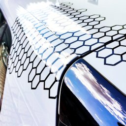 Agencja Promocyjno-Reklamowa SPOT s.c. Piotr Czerwiński, Wojciech Krawczyk - Biały samochód z czarnym, heksagonalnym wzorem na karoserii, odbijającym światło słoneczne.