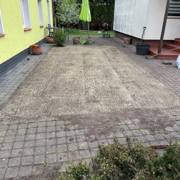 Serwis Ogrodowy Wiśniewski Bartosz Wiśniewski - Przygotowane podłoże pod trawnik z wysianą trawą na podwórku z kostki brukowej, widoczne budynki i elementy ogrodu.