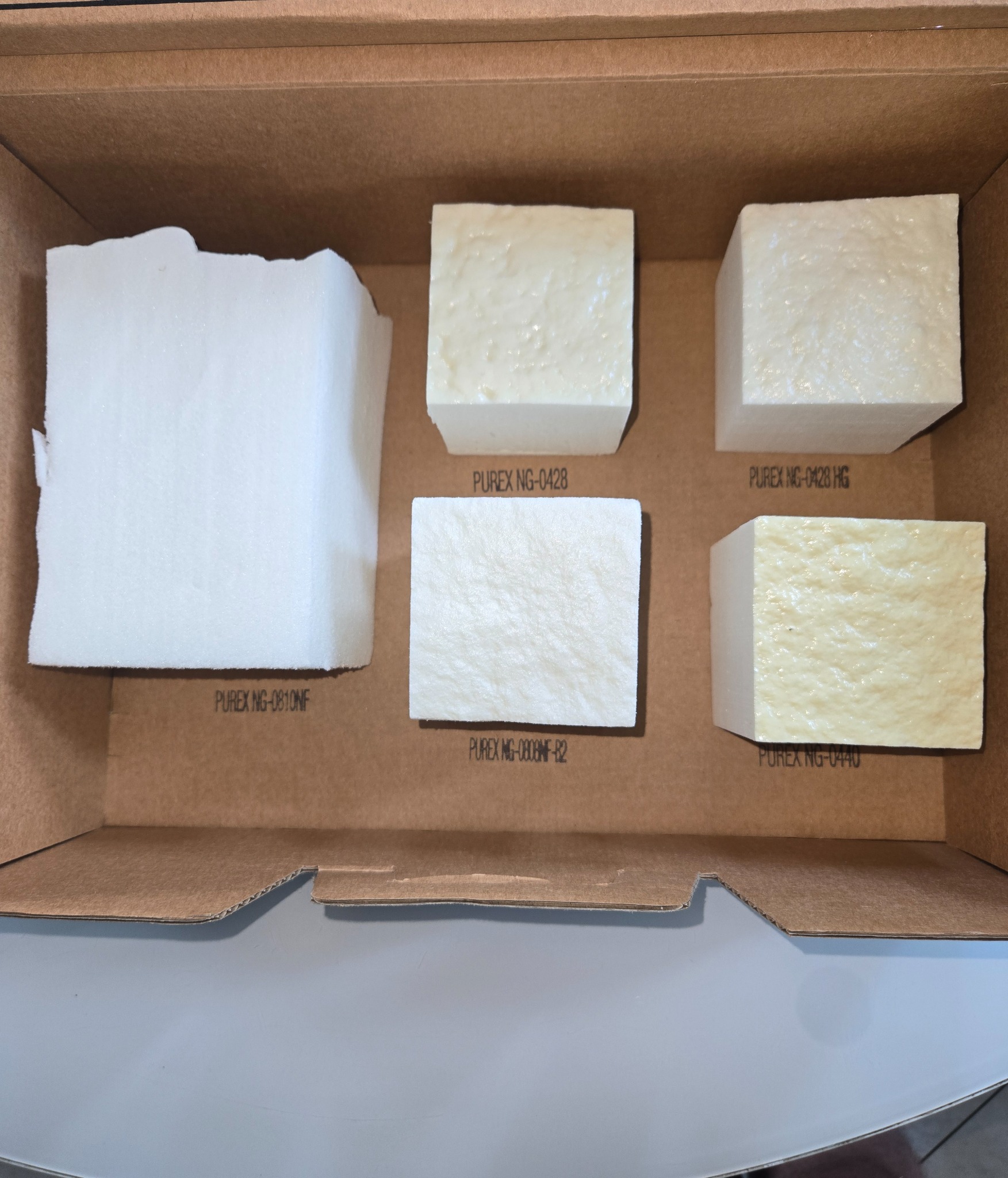 Próbki pianki PUR w kartonowym pudełku, różne gęstości i odcienie, z oznaczeniami producenta PUREX.