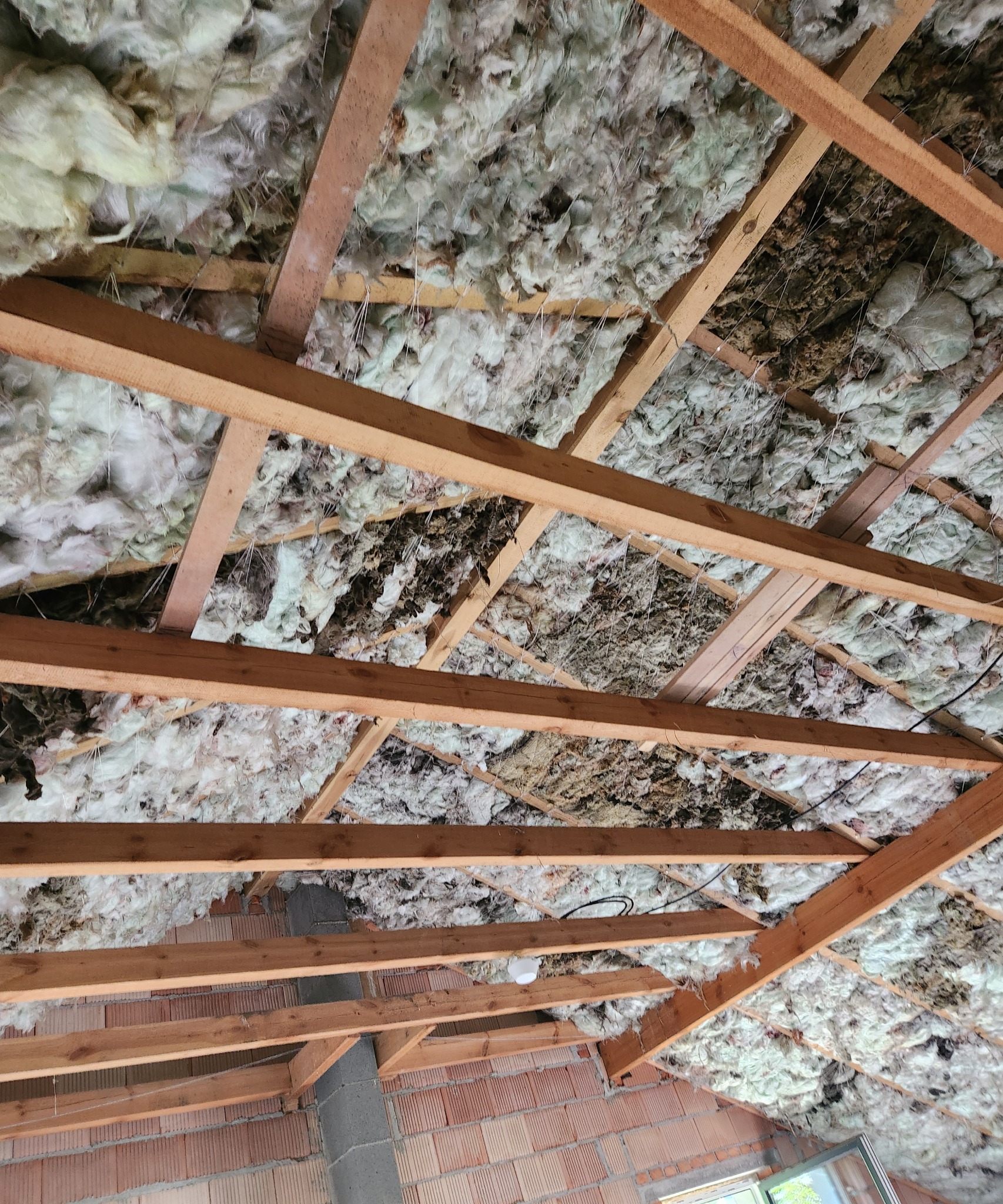 Ocieplenie poddasza pianką PUR pomiędzy drewnianymi krokwiami, widoczna instalacja elektryczna i mur z cegły.