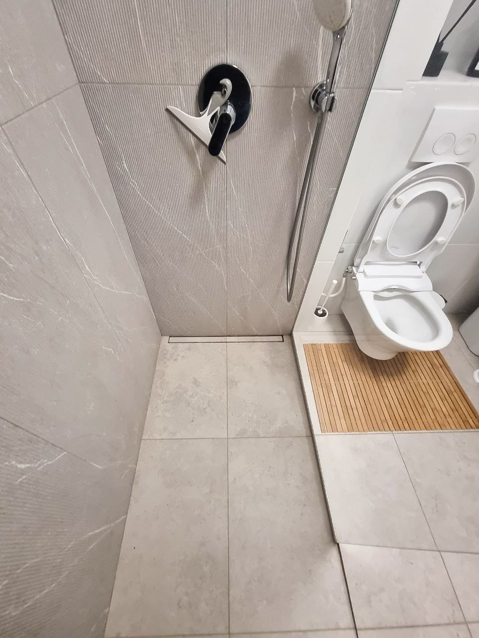 Wykończona łazienka z kabiną prysznicową typu walk-in, armaturą w kolorze chromu i czerni, odpływem liniowym w podłodze oraz toaletą z deską bidetową.