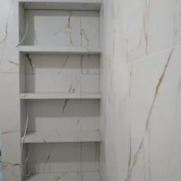 Wnęka z półkami wyłożona białymi płytkami imitującymi marmur, z widocznymi przewodami elektrycznymi, prawdopodobnie przygotowana pod oświetlenie.