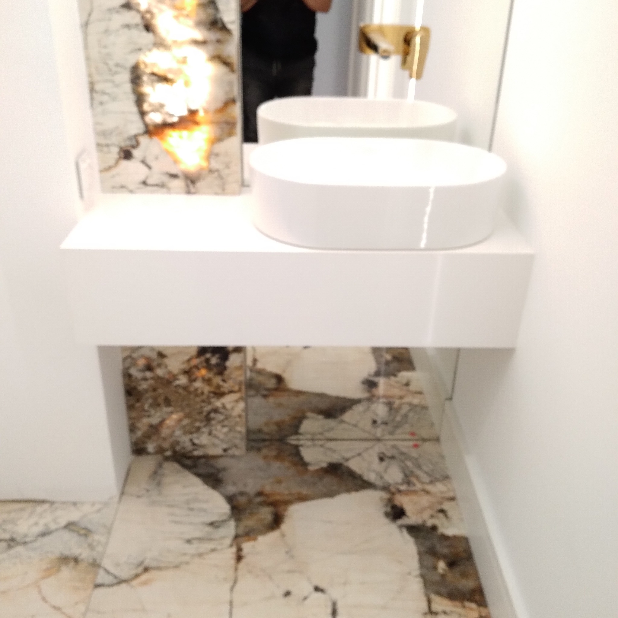 Nowoczesna łazienka z okrągłą umywalką nablatową na białej szafce, marmurowa ściana i podłoga z kontrastującymi żyłami.