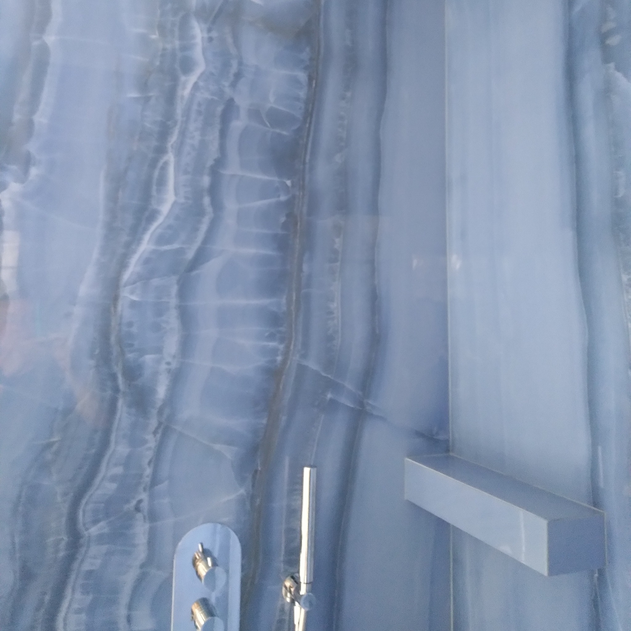 Niebieska ściana z onyksu w kabinie prysznicowej, z chromowaną armaturą i półką, wykonana w Brwinowie.