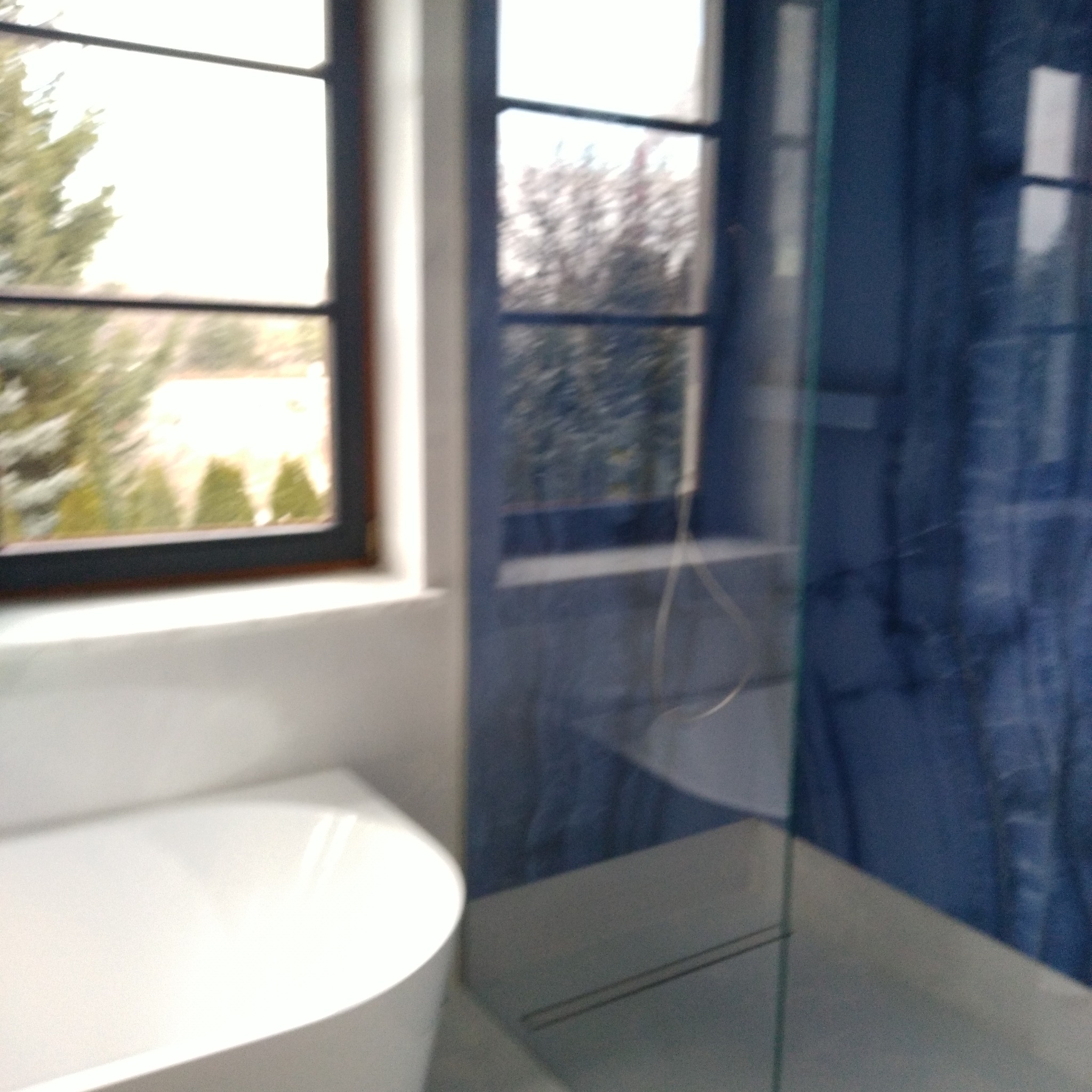 Fragment łazienki z białą wanną narożną, niebieskimi płytkami i oknem z widokiem na zieleń