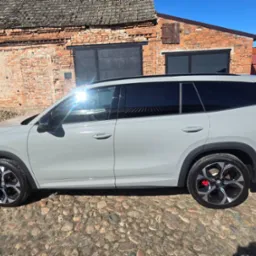 Szary SUV z przyciemnionymi szybami, zaparkowany na brukowanej nawierzchni przed ceglanym budynkiem w słoneczny dzień. Widoczne czerwone zaciski hamulcowe.