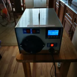 Generator ozonu Bitom z wyświetlaczem czasu pracy i przełącznikami, ustawiony na drewnianym stoliku, z widocznym kablem zasilającym i gniazdkiem.