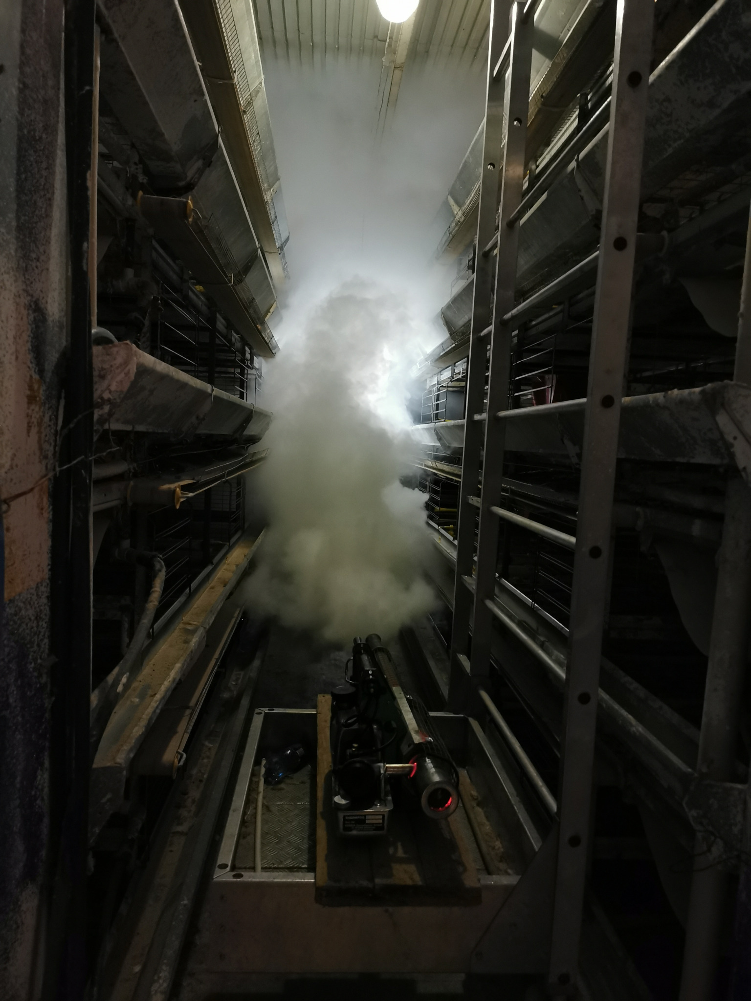 Zamglenie wewnątrz budynku z metalową konstrukcją i drabiną, prawdopodobnie w trakcie zabiegu dezynfekcji lub deratyzacji.