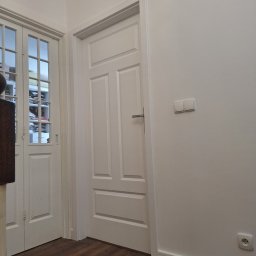 Ivan Katrych - Jasne wnętrze z dwiema parami białych drzwi: pełne i przeszklone. Podłoga z paneli w odcieniach brązu. Minimalistyczny design, gładkie, białe ściany.