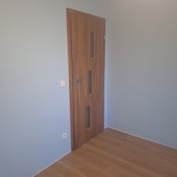 Ivan Katrych - Wnętrze po remoncie: drewniane panele podłogowe, pomalowane na jasny kolor ściany i zamontowane drzwi z przeszkleniami. Widoczne gniazdka i włącznik.