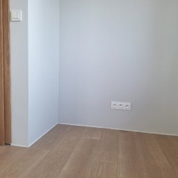 Ivan Katrych - Pomalowane na szaro wnętrze pokoju z drewnianą podłogą i drzwiami. Widoczne gniazdka elektryczne i włącznik światła. Minimalistyczny design.