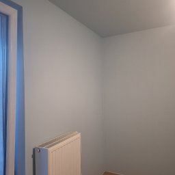 Ivan Katrych - Jasny pokój po malowaniu ścian na pastelowy odcień błękitu, z widocznym grzejnikiem i fragmentem podłogi z paneli. Świeżo pomalowane ściany.