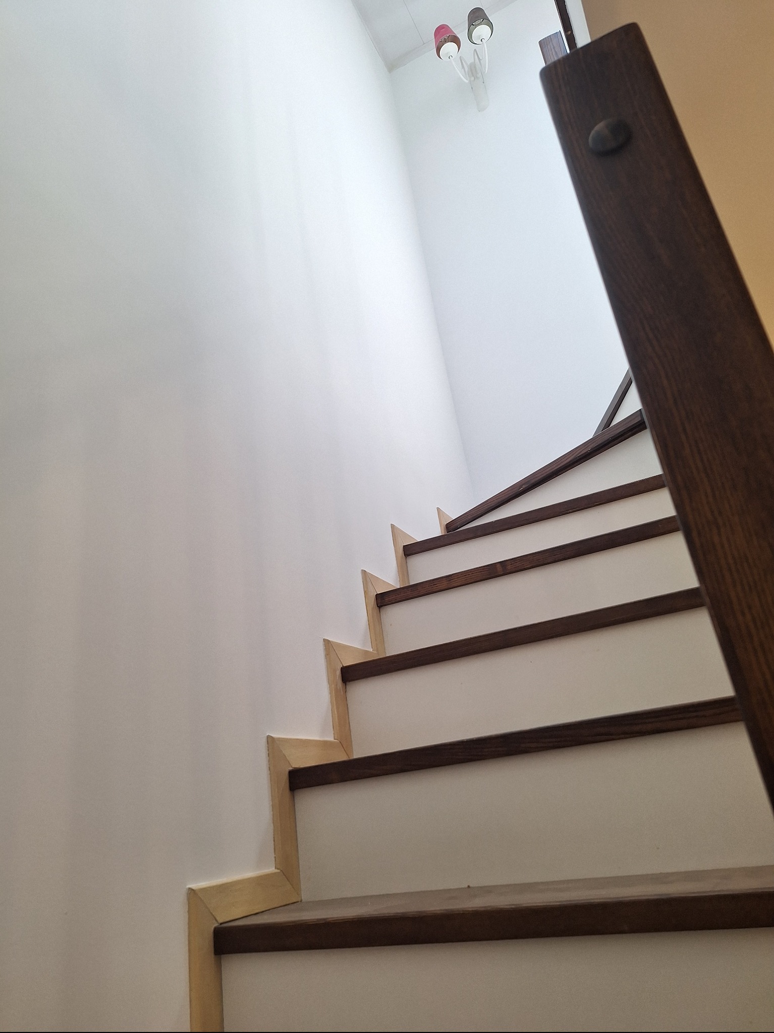 Nowoczesne schody drewniane z białymi podstopnicami w Piasecznie. Widoczne detale wykończenia i oświetlenie sufitowe. Ujęcie z dołu podkreśla geometrię konstrukcji.