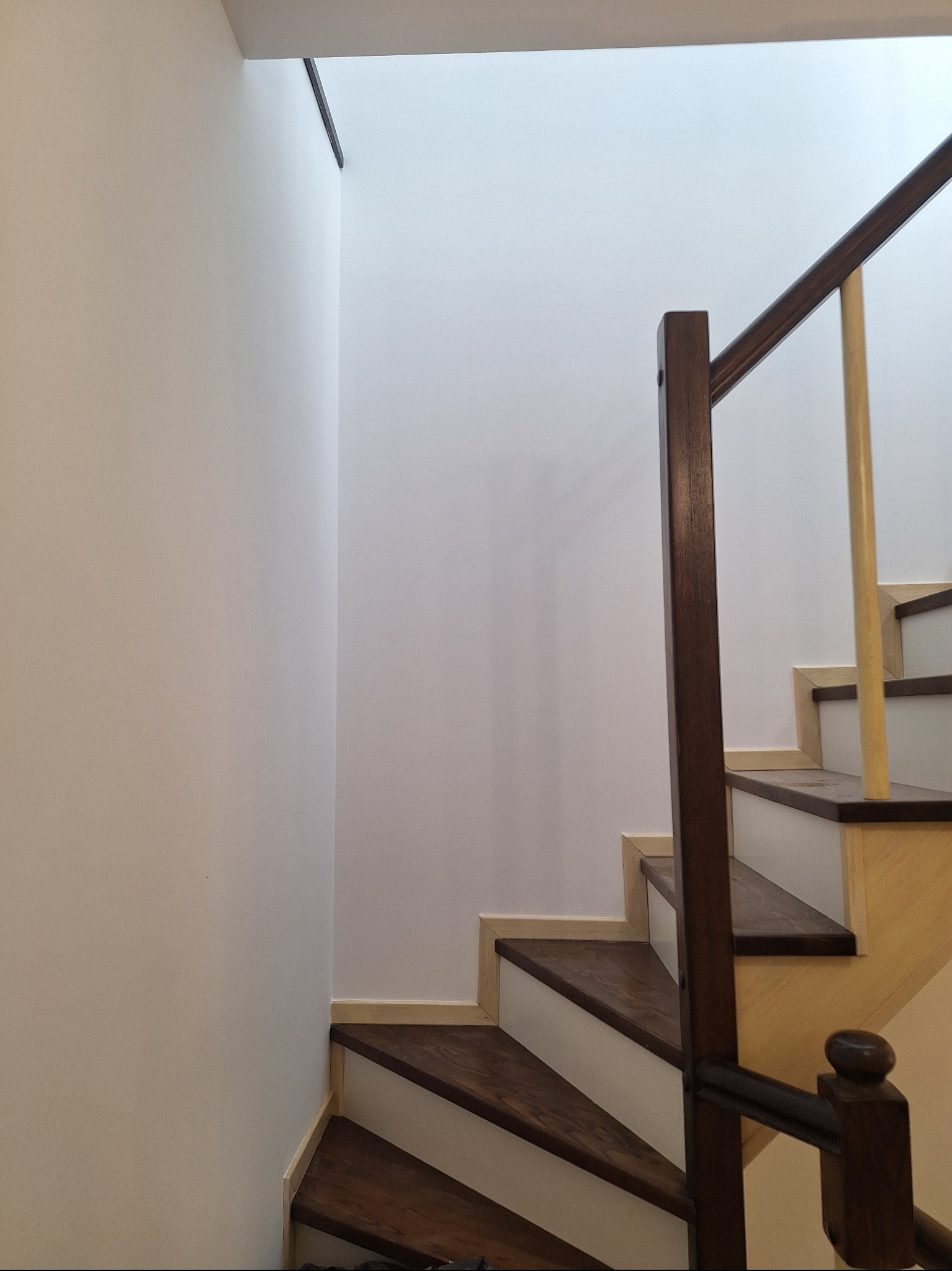 Wnętrze domu: schody z drewnianymi stopniami i białą balustradą, oświetlone światłem dziennym wpadającym z góry. Ściany pomalowane na jasny, neutralny kolor.