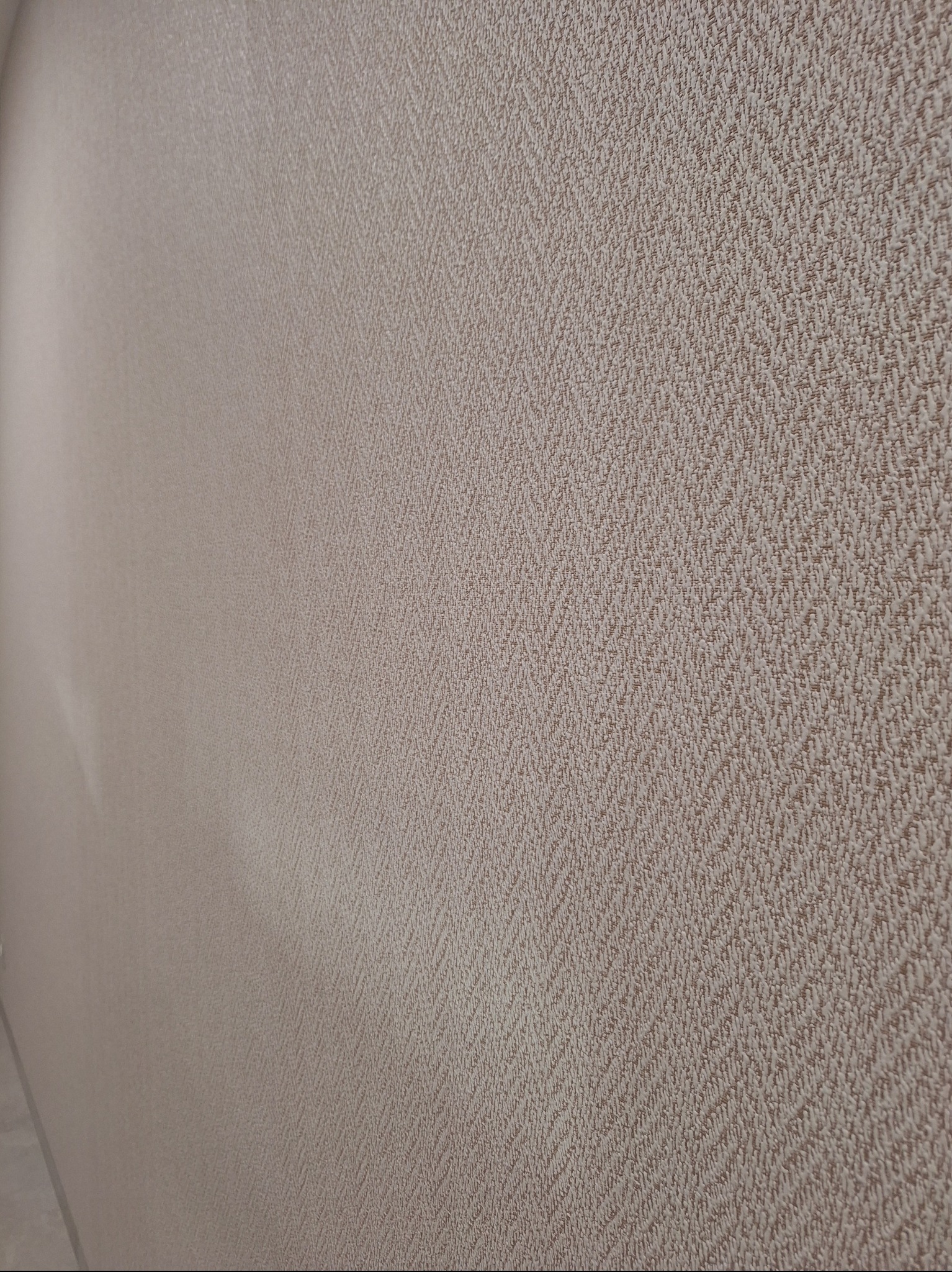 Beżowa ściana z wyraźną, teksturowaną tapetą w jodełkę, sfotografowana pod kątem, ukazująca detale faktury i subtelne przejścia tonalne.