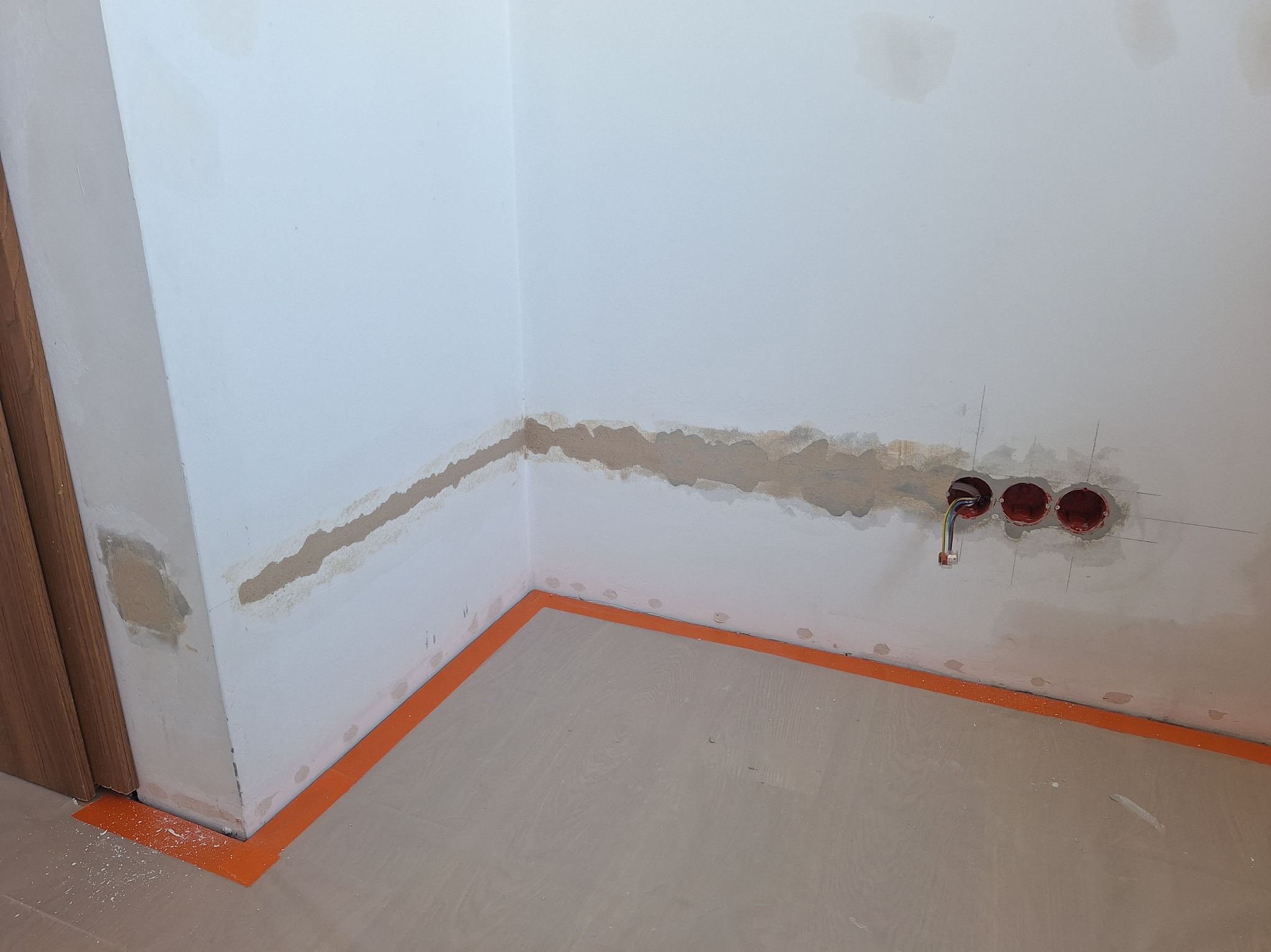 Przygotowanie ściany do malowania: fragment ściany z widocznymi śladami po szpachlowaniu, zabezpieczona podłoga, gniazdka elektryczne z wystającymi kablami.