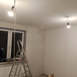 R.D. - Bud Budowa - Remonty RAFAŁ SKATUŁA - Pokój w trakcie prac wykończeniowych: drabina, gładzie gipsowe, prowizoryczne oświetlenie. Ściany częściowo pokryte gładzią, widoczne narzędzia i materiały budowlane.