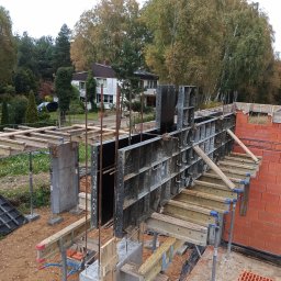 R.D. - Bud Budowa - Remonty RAFAŁ SKATUŁA - Wysoka perspektywa na szalunek fundamentów z metalowymi panelami i drewnianymi belkami, częściowo zabetonowany, z widocznymi prętami zbrojeniowymi i fragmentem murowanej ściany.