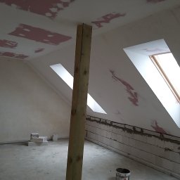 PN-BUD PAWEŁ NOWAK - Poddasze w trakcie remontu: ściany z bloków połączonych zaprawą, częściowo pokryte szpachlą, sufit z widocznymi łatami szpachli, drewniany słup podtrzymujący, okna dachowe, na podłodze resztki...