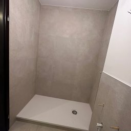 PN-BUD PAWEŁ NOWAK - Wykończona kabina prysznicowa z beżowymi płytkami, widoczne niedokończone przyłącza wodne. Minimalistyczny design, jasne oświetlenie.